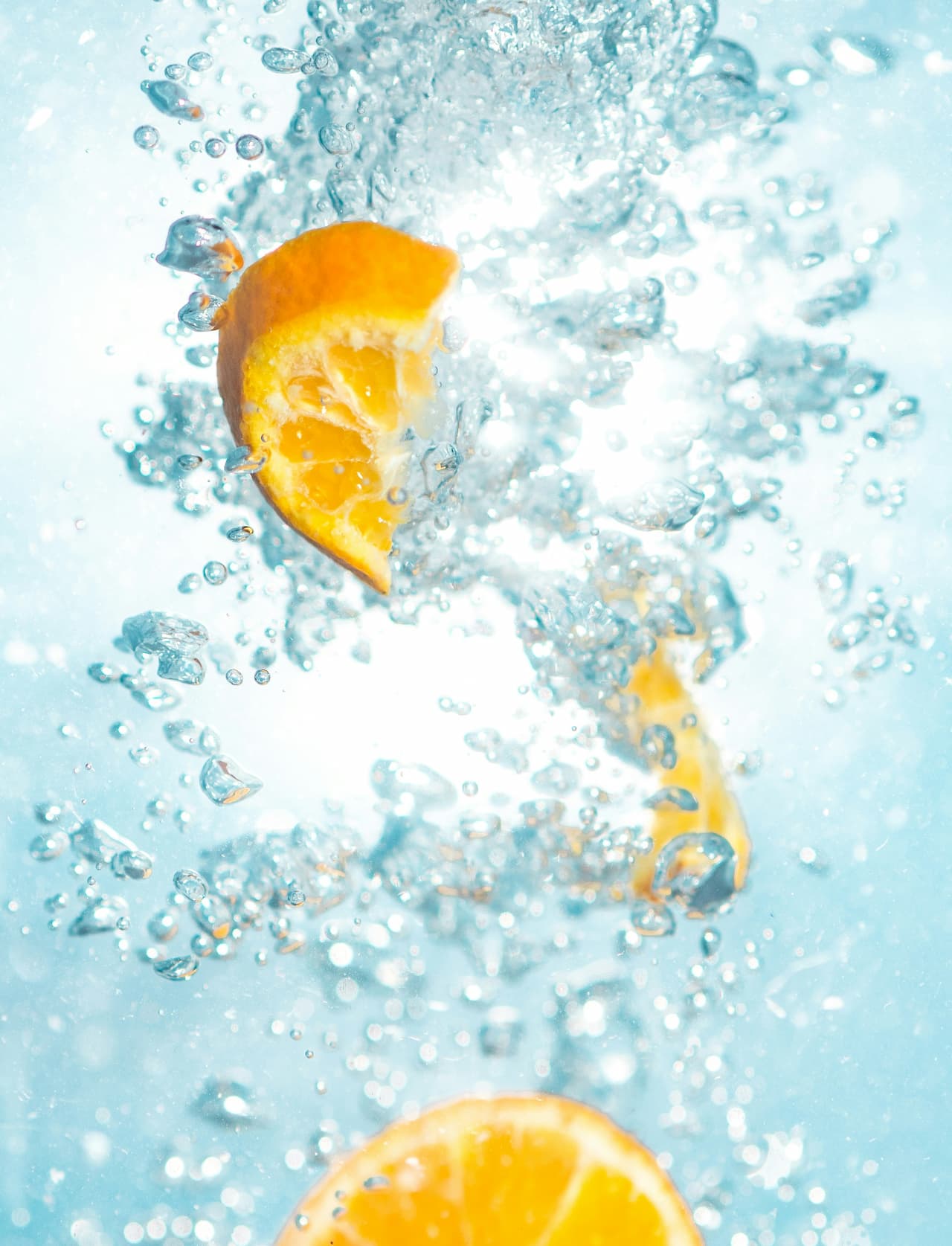 A cut orange being dropped in refreshing cold water